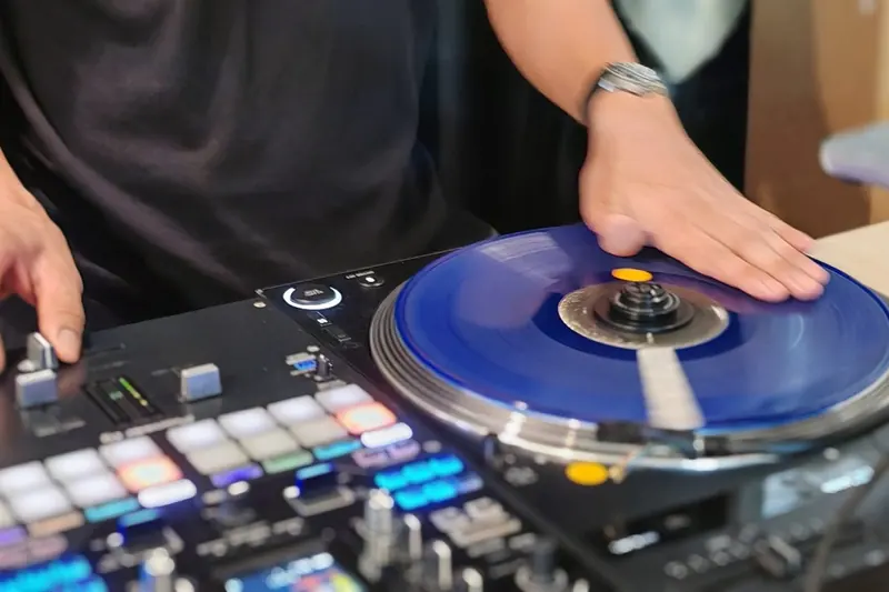 มือวางบนจานเสียงสีน้ำเงินของเครื่อง DJ